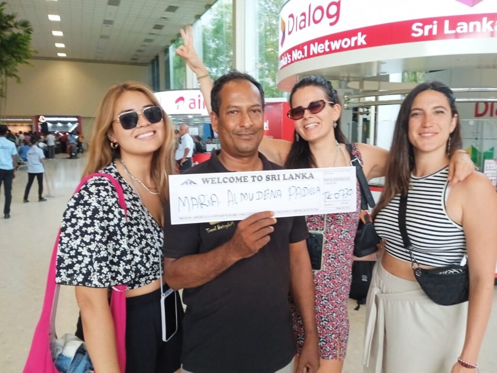 A man holds a sign reading “Maria Almudena Padua” at an airport arrivals area, standing with three women posing for a photo.