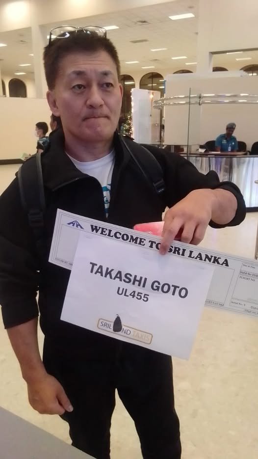 A man holds a sign reading “Maria Almudena Padua” at an airport arrivals area, standing with three women posing for a photo.